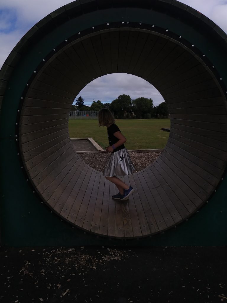 A girl running on a playground tube like a hamster wheel
